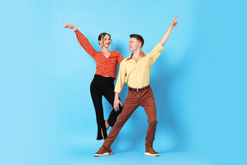 Happy couple in retro outfits dancing on light blue background