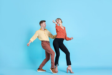 Happy couple in retro outfits dancing on light blue background