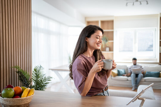Smiling woman drinking coffee and using tablet in modern apartment