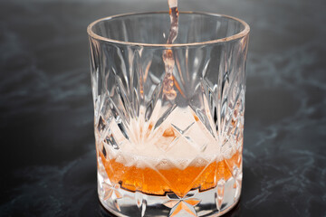 A vibrant orange beverage is being poured into a beautifully cut crystal glass. The drink creates...