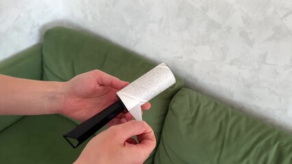 Man changes sticky layer new one. Sticky roller for dust, hair and wool cleaning. Cleaning green sofa with a roller