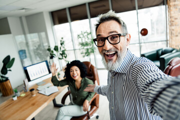 Energetic colleagues taking selfie together in a bright modern office environment, embodying...