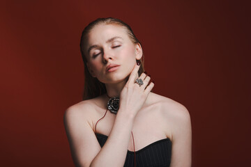 Beautiful woman in stylish necklace and ring posing on dark red background