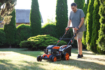 Man cutting green grass with lawn mower in garden