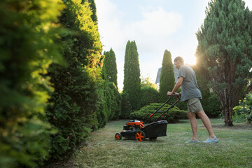 Man cutting green grass with lawn mower in garden