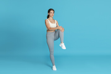 Fototapeta premium Teenage girl in sportswear stretching on light blue background