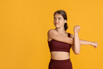 Teenage girl in sportswear stretching on orange background, space for text