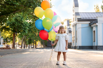 Cute little girl in dress with bunch of colorful balloons outdoors at sunset
