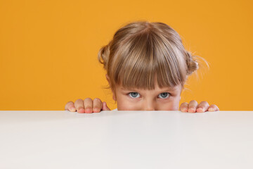 Curious little girl peeking over table against orange background