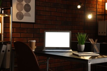 Laptop, takeaway paper cup, houseplants and stationery on black table near brick wall