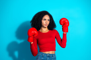 Young stylish woman wearing red boxing gloves in a confident pose against a vivid blue background