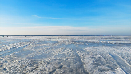 Vast icy landscape with distant ice fishermen enjoying a winter day on frozen lake