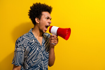 Young stylish man using a megaphone to express an emotion against a vibrant yellow background