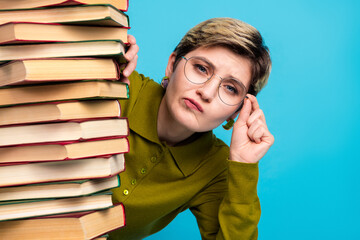 Young woman with short hair and glasses posing with stack of book against a vibrant blue background