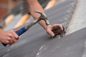 Roofing conctractror working on steep roof, carefully nailing down slate tiles while ensuring proper alignment