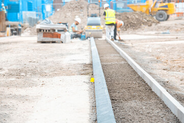 Construction workers installing pavement alongside a new sidewalk in a city area