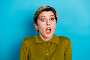 Surprised young woman in fashionable green shirt and glasses expressing amazement against vibrant...