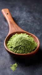 Wooden spoon holding green matcha powder on dark background