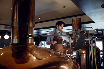 Brewer man wearing an apron is diligently working on a copper machine