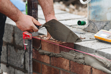 Close-up of Skilled bricklayer laying bricks with trowel on construction site