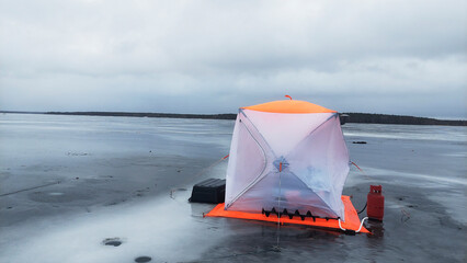 Ice fishing shelter sits alone on a frozen lake as clouds dominate the overcast sky in winter