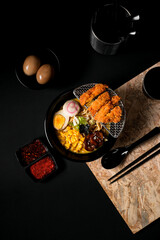 Chicken ramen topped with crispy chicken katsu, sweet corn, marinated egg, narutomaki, seaweed, and sesame seeds served in rich chicken broth. black background.