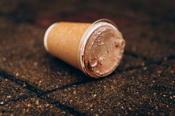 Used takeaway coffee cup discarded on city street after rainfall