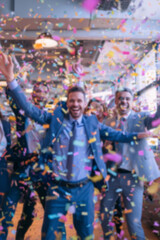 Obraz premium Blurred background of people in business suits celebrating in an office, throwing confetti and holding party streamers. Concept of corporate celebration, team success, and joyful workplace moments.