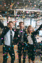 Fototapeta premium Blurred background of people in business suits celebrating in an office, throwing confetti and holding party streamers. Concept of corporate celebration, team success, and joyful workplace moments.