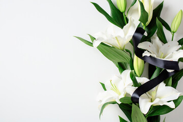 White lilies with black ribbon on white background. Minimalist floral arrangement symbolizing mourning, purity, and remembrance in a serene, elegant style.