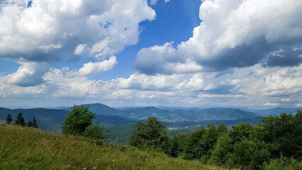 A stunning view of a lush mountain range under a bright blue sky with rolling clouds, perfect for...