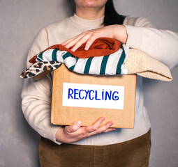 Woman holding cardboard box full of clothes labeled Recycling. Concept of sustainable fashion and...