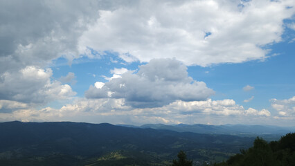 A stunning view of a lush mountain range under a bright blue sky with rolling clouds, perfect for...