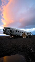 A crashed plane on a black sand beach at sunset
