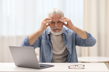 Senior man suffering from headache at table indoors