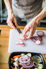 Hands cutting onion and radish for fresh vegetable salad.