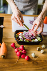 Hands cutting onion and radish for fresh vegetable salad.