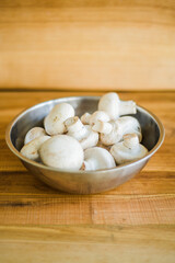 Fresh white mushrooms in a metal bowl on wooden background.
