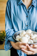 Fresh white mushrooms in a metal bowl on wooden background.