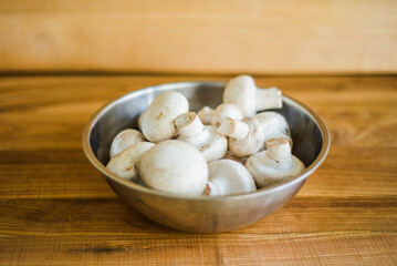 Fresh white mushrooms in a metal bowl on wooden background.