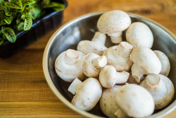 Fresh white mushrooms in a metal bowl on wooden background.