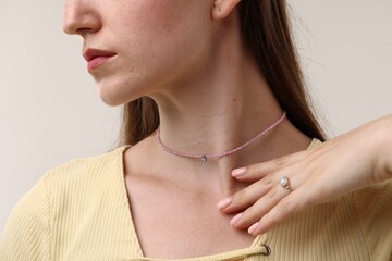 Woman wearing stylish necklace on light grey background, closeup