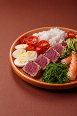 Seafood bowl, tuna tataki fillet slices with rice, oranges, tomatoes and sauce. Tuna bowl