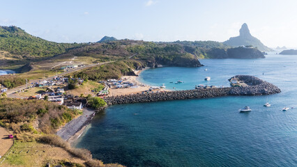 Visão aérea da Praia do Porto em Fernando de Noronha, com barcos ancorados e mar de tons azuis. © RNL Fotografia