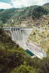 Massive concrete dam with spillways and hydroelectric facility nestled in a mountainous forested...