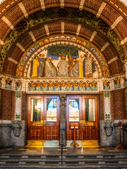 Main entrance of Copenhagen City Hall with ornate brick archway, mosaic of historical figures, floral motifs, and wooden doors under clear daylight.