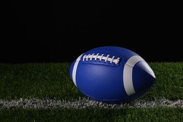 Obraz premium A textured American football resting on the green artificial turf with white line. College Football