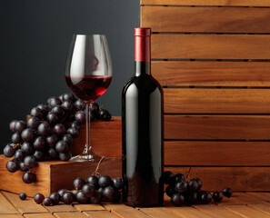Bottle and glass of red wine and blue grapes on a wooden background.
