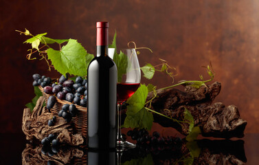 Glass and bottle of red wine with blue grapes and vine branches.