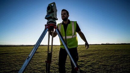 Man land surveyor in reflective vest working with total station equipment outdoors on a sunny field, surveying footage.